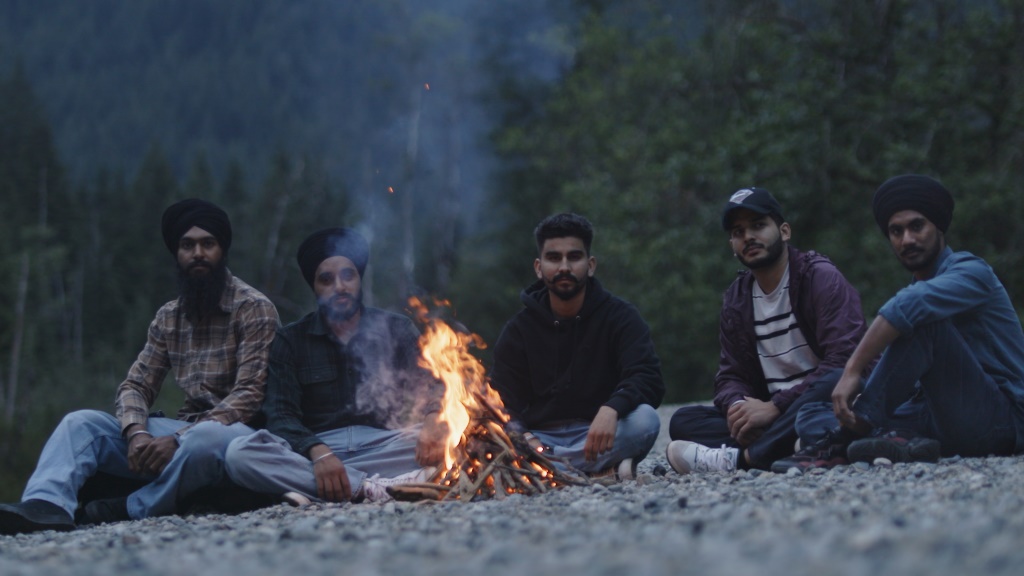 Gurpreet Singh, Gagandeep Singh, Arvindjeet Singh, Ajay Kumar, and Kuljinder Singh sit in front of a fire in Golden Ears Provincial Park, where they performed an incredible rescue of two fallen hikers. They stare directly into the camera.