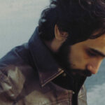 An archival photo of Dr. Gabor Maté. He is wearing a brown leather jacket and standing on a beach.