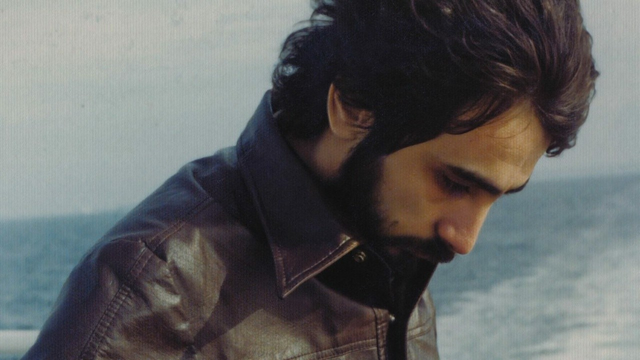 An archival photo of Dr. Gabor Maté. He is wearing a brown leather jacket and standing on a beach.