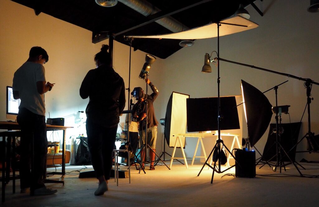A film crew sets up a shot on set. They are preparing lighting and viewed in silhouette.