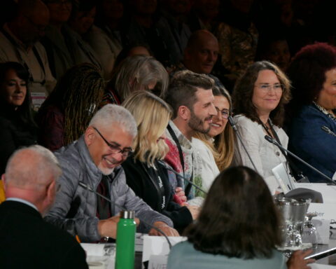 A diverse group of professionals at an industry conference sits at a board table. They are having an engaged conversation.