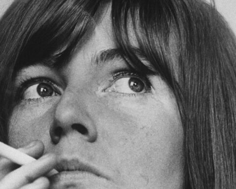 A black and white portrait of Irish author Edna O'Brien. She is framed in close-up while smoking a cigarette.