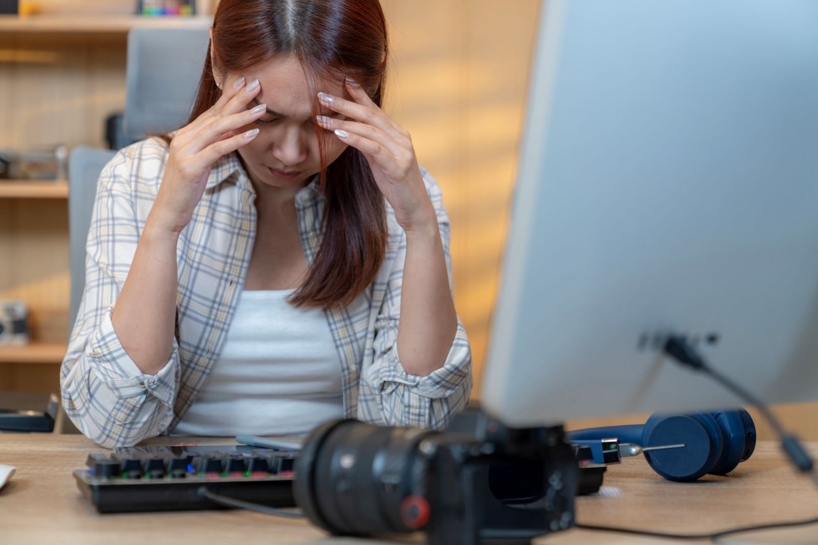 A woman sits at her computer with her hands on her forehead, indicating that she had a headache.