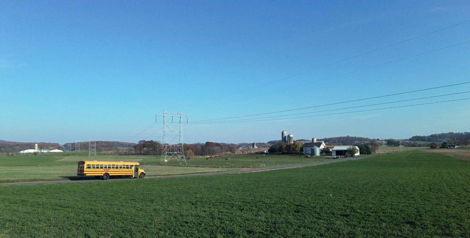 An orange school bus is parked beside a green field. The sky is blue and clear.