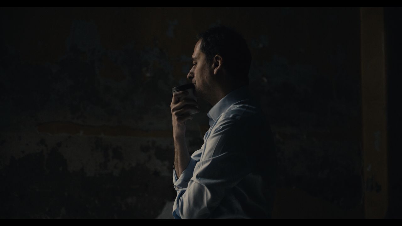 Bulgarian journalist Christo Grozev stands in pensive thought. The room is very dark. There is some light on his hand and face. He is wearing a white shirt.