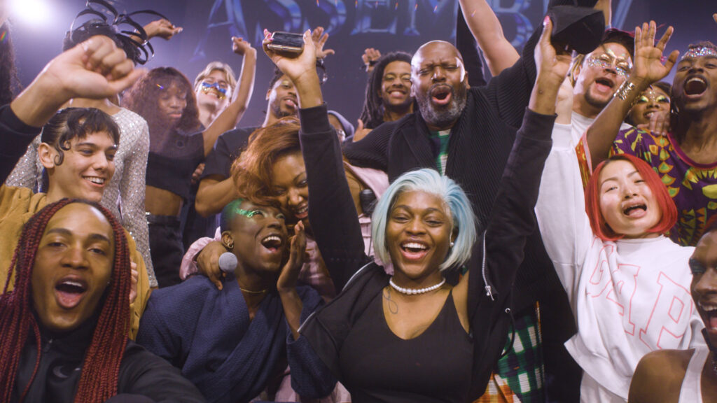 A group shot of Black artists and performers sharing a moment of joy. They are mostly wearing black shirts and have their hands in the air.
