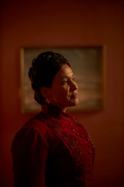 A Métis woman wears an old red dress with her hair up.