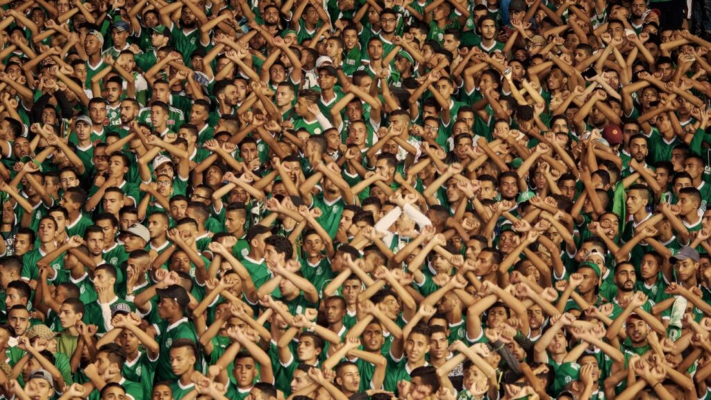 A stadium full of fans. They all have their arms over their heads crossed as an X.