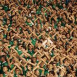 A stadium full of fans. They all have their arms over their heads crossed as an X.