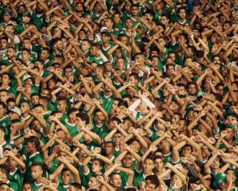 A stadium full of fans. They all have their arms over their heads crossed as an X.