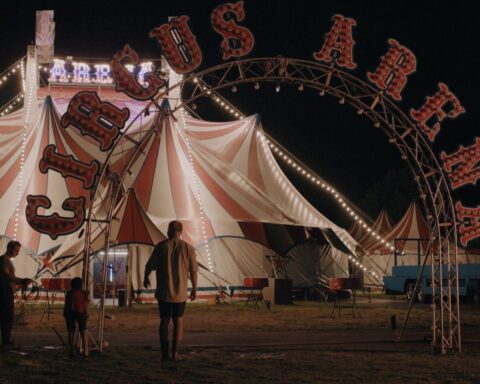 A boy approaches a circus tent at night. The words Circus Arena appear in red on an arch above the entrance.