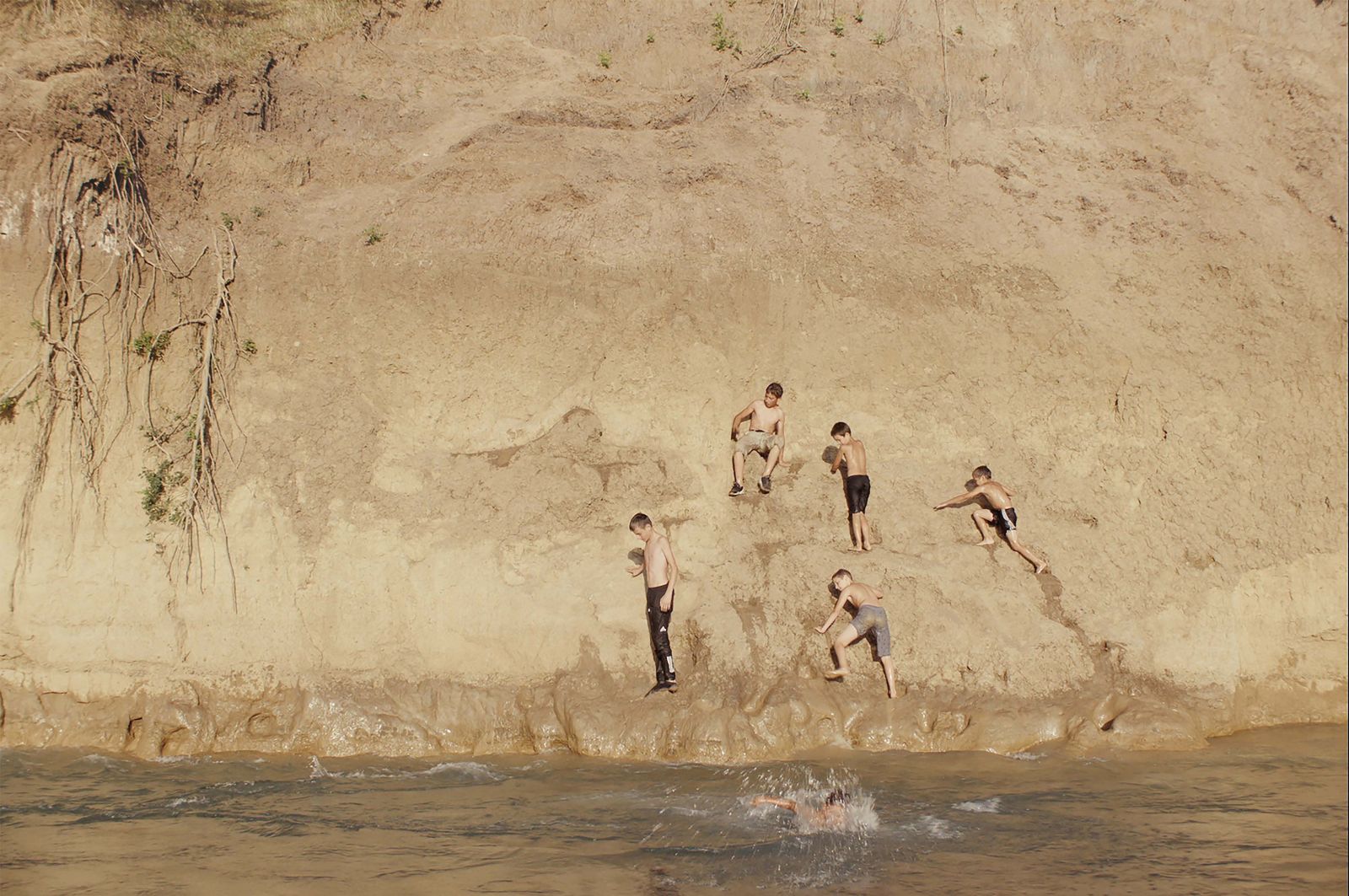 Five young boys play on a rocky shoulder near a pond.