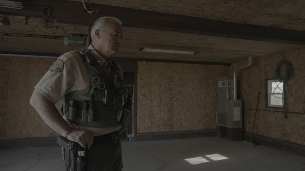 A police officer stands with his hands on his hips in a garage.