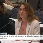 NFB Chairperson Suzanne Guevremont is a Caucasian woman wearing a white blazer. She has blond hair and is seated at a microphone at a grey table.