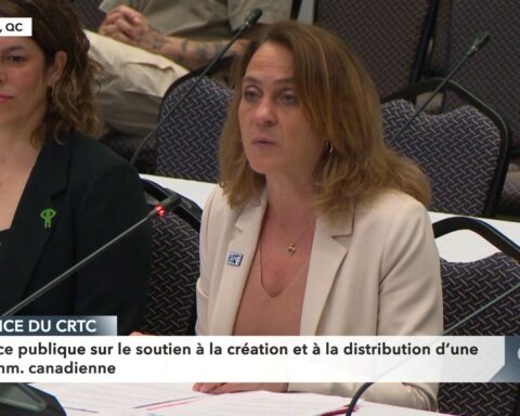 NFB Chairperson Suzanne Guevremont is a Caucasian woman wearing a white blazer. She has blond hair and is seated at a microphone at a grey table.