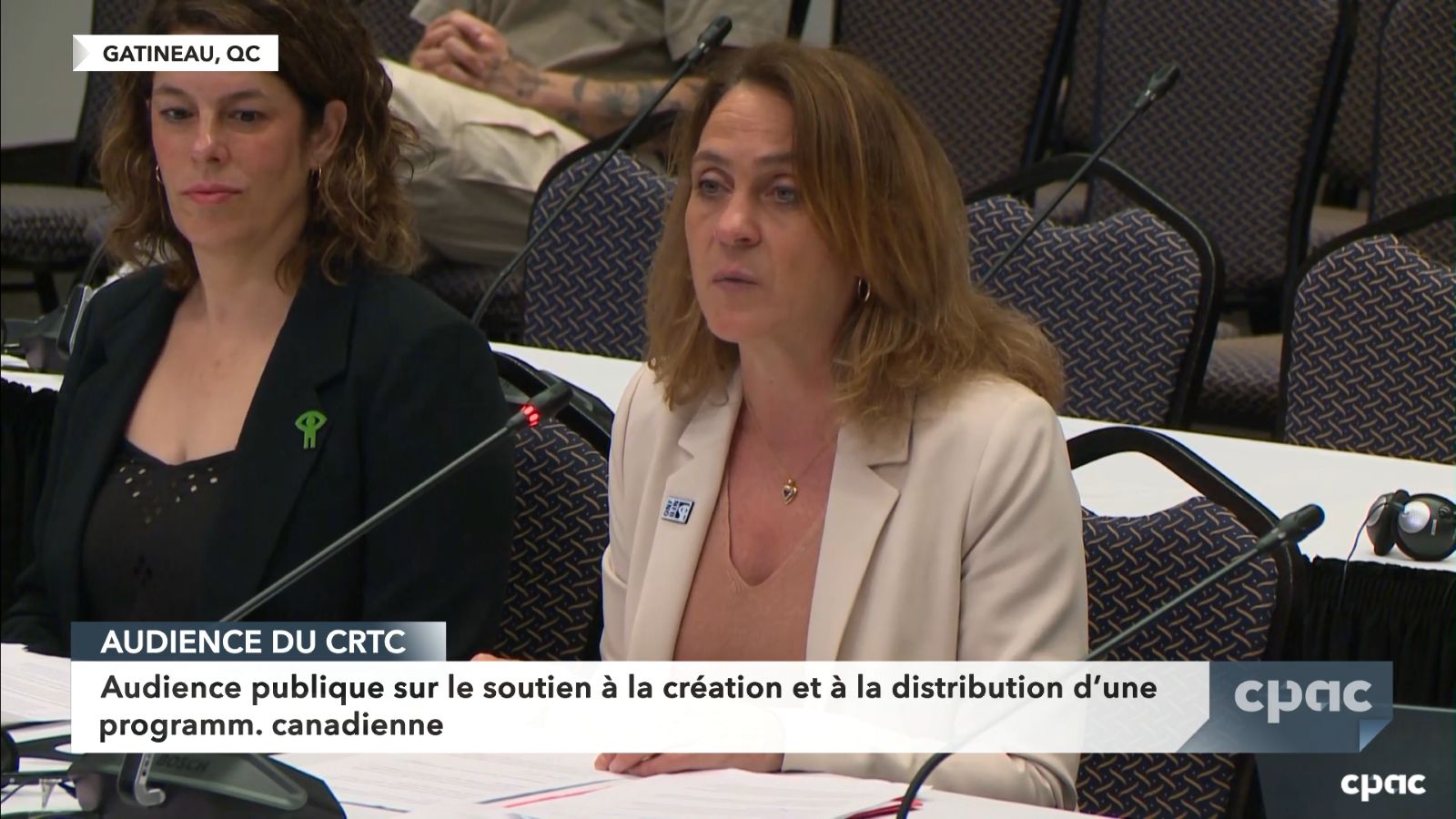 NFB Chairperson Suzanne Guevremont is a Caucasian woman wearing a white blazer. She has blond hair and is seated at a microphone at a grey table.