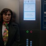 Manizha Bakhtari, an Afghan woman, stands in an elevator. She is wearing a dark suit with a pink and yellow checkered scarf.