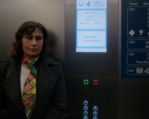 Manizha Bakhtari, an Afghan woman, stands in an elevator. She is wearing a dark suit with a pink and yellow checkered scarf.