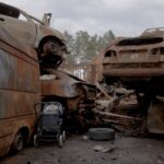 An abandoned stroller sits amid a heap of rusted cars destroyed by Russian violence in Ukraine.