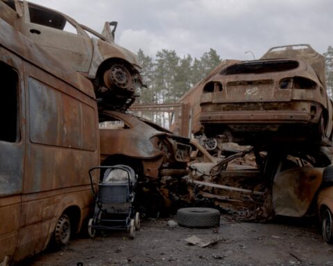 An abandoned stroller sits amid a heap of rusted cars destroyed by Russian violence in Ukraine.