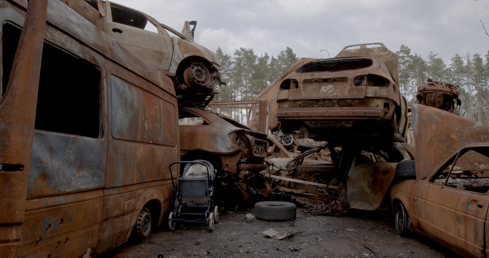 An abandoned stroller sits amid a heap of rusted cars destroyed by Russian violence in Ukraine.