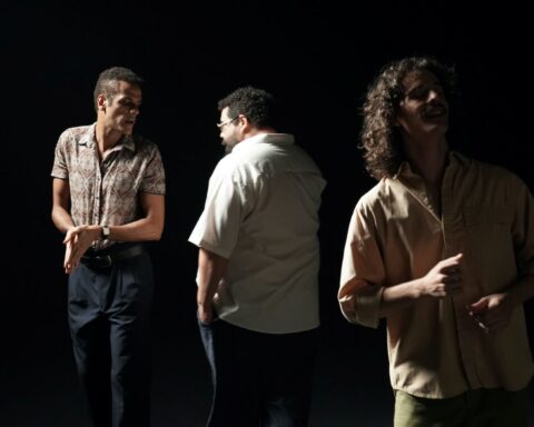 Three actors appear on a black stage. They have spotlights on them and are interacting.