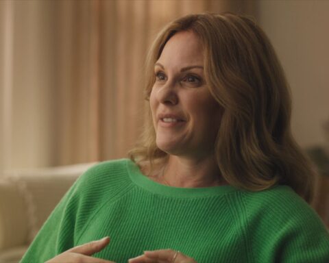 Heather is a white woman with blond hair and brown eyes. She is seated giving an interview. She is wearing a green sweater and seated in front of a window with white curtains.