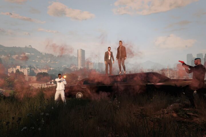 Four players are pictured in the video game Grand Theft Auto. Two stand atop a hill, and then there is a player on either side of them. The players to the sides have their guns drawn.
