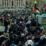 A crowd of student protesters on the grounds at Columbia University. A Palestinian flag is visible in the centre of the group.