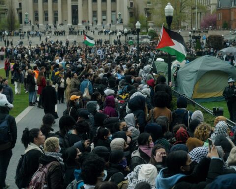 A crowd of student protesters on the grounds at Columbia University. A Palestinian flag is visible in the centre of the group.