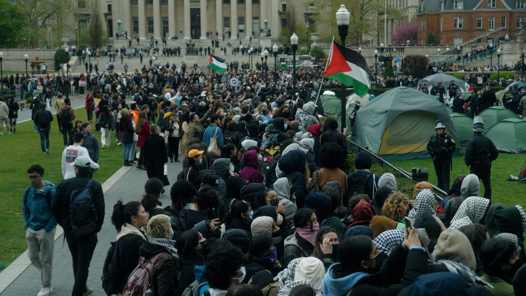 A crowd of student protesters on the grounds at Columbia University. A Palestinian flag is visible in the centre of the group.