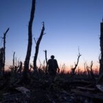 Ukrainian servicemen walk through charred forest a few kilometers from Andriivka, Donetsk region, Ukraine. The sun has set and the soldier walks towards the horizon.