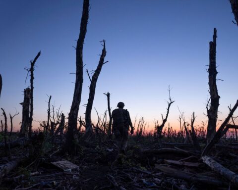 Ukrainian servicemen walk through charred forest a few kilometers from Andriivka, Donetsk region, Ukraine. The sun has set and the soldier walks towards the horizon.