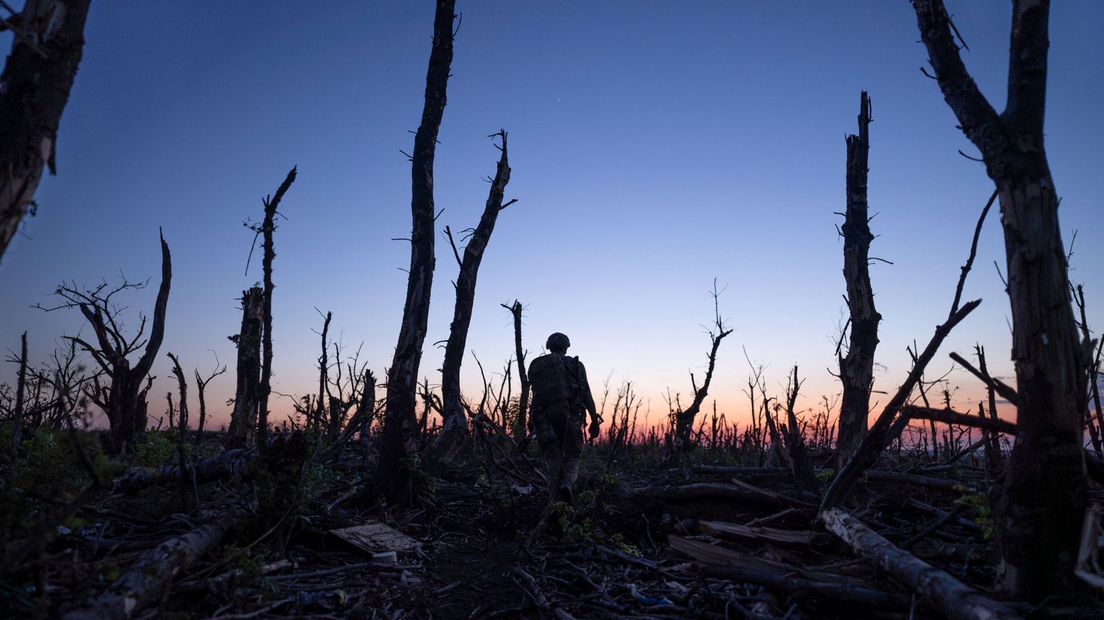 Ukrainian servicemen walk through charred forest a few kilometers from Andriivka, Donetsk region, Ukraine. The sun has set and the soldier walks towards the horizon.