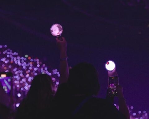 Fans hold up lights at a BTS concert. The view shows a crowd of young people bathed in purple light.