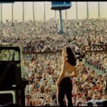 An archival photo of singer Paula Cole at Lilith Fair. She is on stage, viewed from behind, and the photo shows her looking out at the crowd of people.