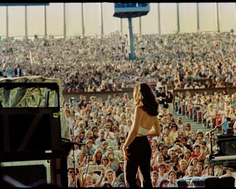 An archival photo of singer Paula Cole at Lilith Fair. She is on stage, viewed from behind, and the photo shows her looking out at the crowd of people.