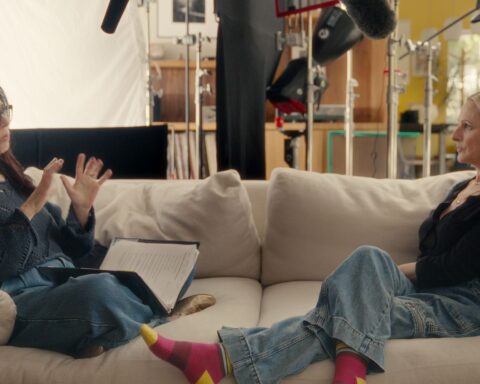 Two women sit at opposite ends of a couch. They are facing each other and having a conversation in American Sign Language.