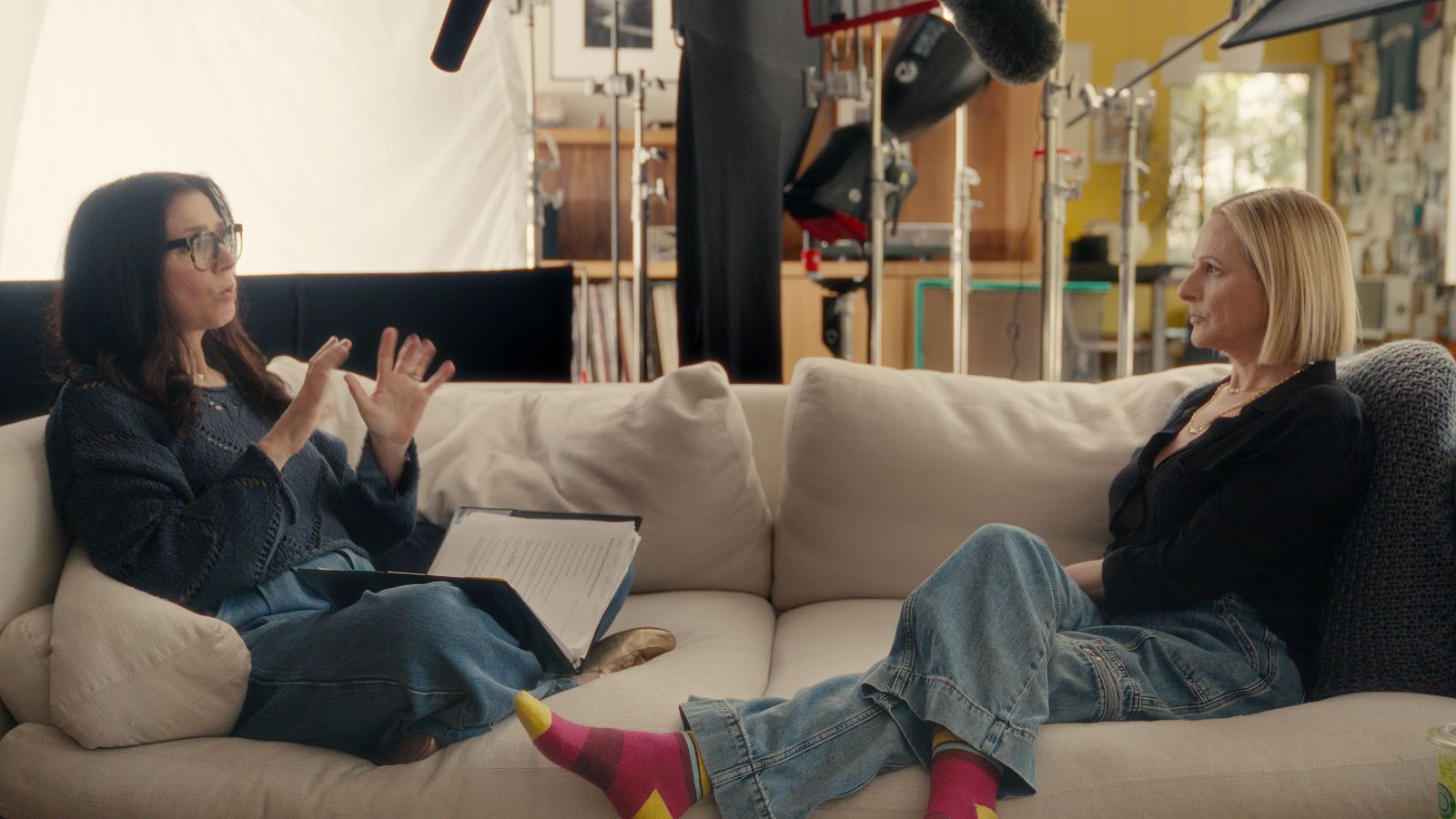 Two women sit at opposite ends of a couch. They are facing each other and having a conversation in American Sign Language.
