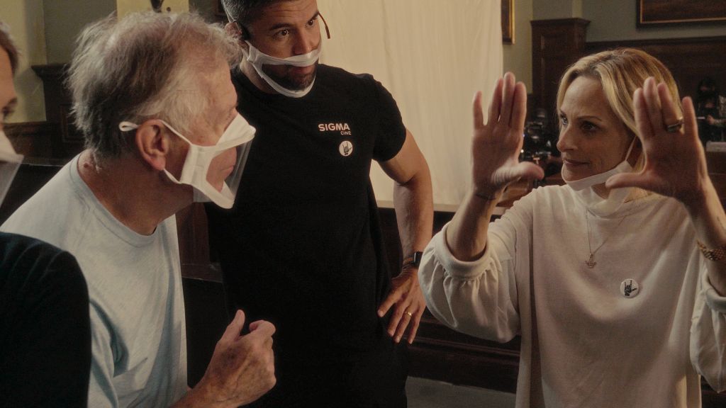 Marlee Matlin directs an actor on a TV shoot. Her hands are raised in the air to express framing. The actor is wearing a face mask with a transparent layer above his mouth so that she can read his lips.