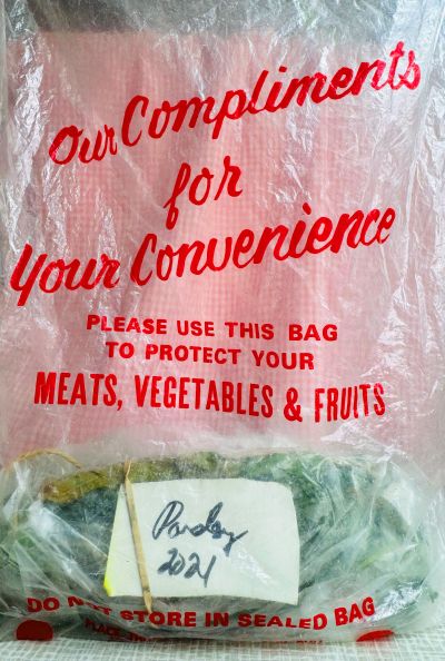 An old white bag with red letters reads: "Our compliments for your convenience. Please use this bag to protect your meat, vegetables, and fruits.' Below it is a hand written label that says 'Parsley, 2021'.