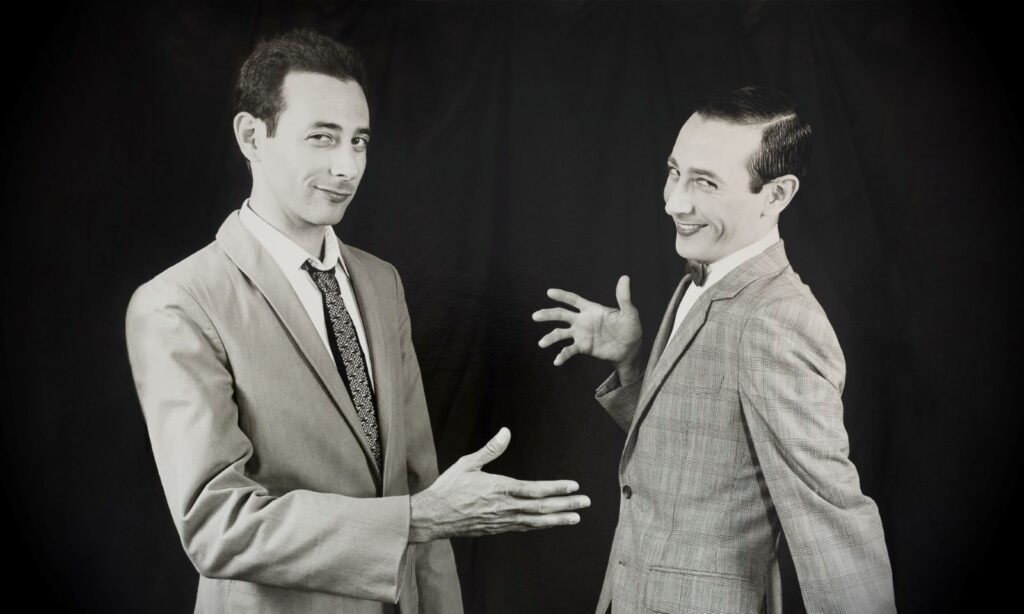 A black and white image of two Pee-Wee Hermans. They are laughing and in the process of giving a high-five.