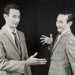 A black and white image of two Pee-Wee Hermans. They are laughing and in the process of giving a high-five.