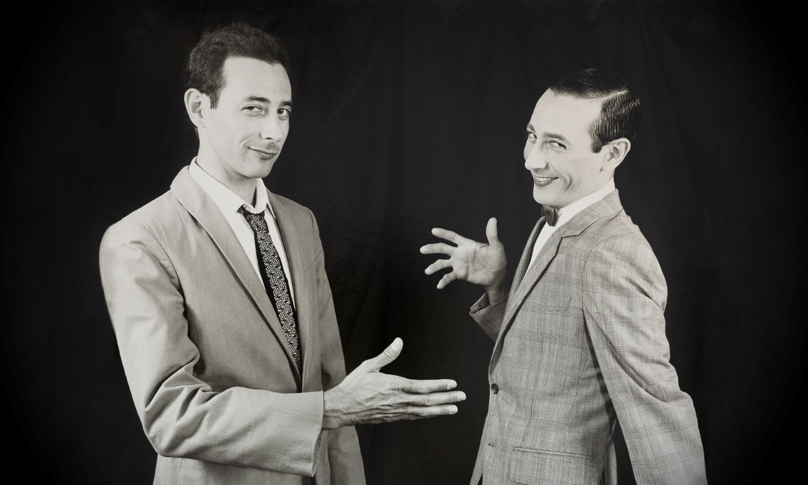 A black and white image of two Pee-Wee Hermans. They are laughing and in the process of giving a high-five.