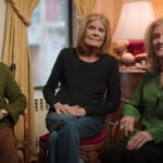 Suzanne Braun Levine (a woman with blond hair and wearing an olive green shirt), Gloria Steinem (with grey-brown hair and wearing a black sleeved shirt with blue jeans), and Letty Cottin Pogrebin (with blond hair, a dark green shirt, and black pants) are seated in a row facing the camera.