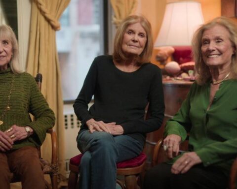 Suzanne Braun Levine (a woman with blond hair and wearing an olive green shirt), Gloria Steinem (with grey-brown hair and wearing a black sleeved shirt with blue jeans), and Letty Cottin Pogrebin (with blond hair, a dark green shirt, and black pants) are seated in a row facing the camera.
