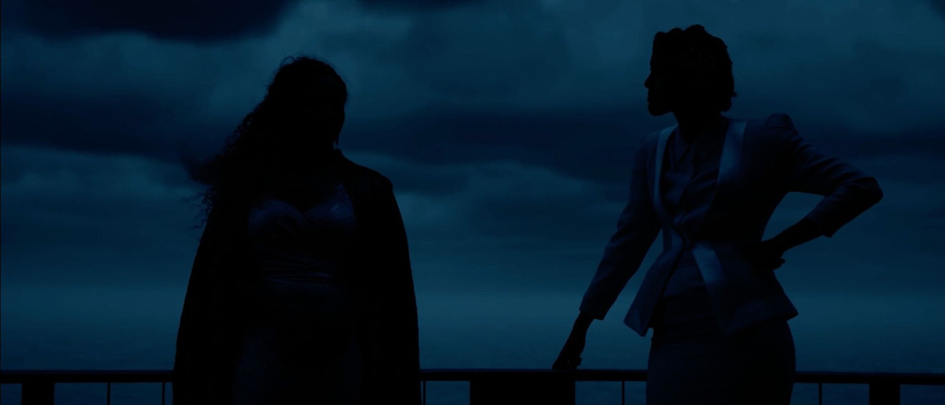 Two figures appear as black silhouettes against a darkened blue backdrop.