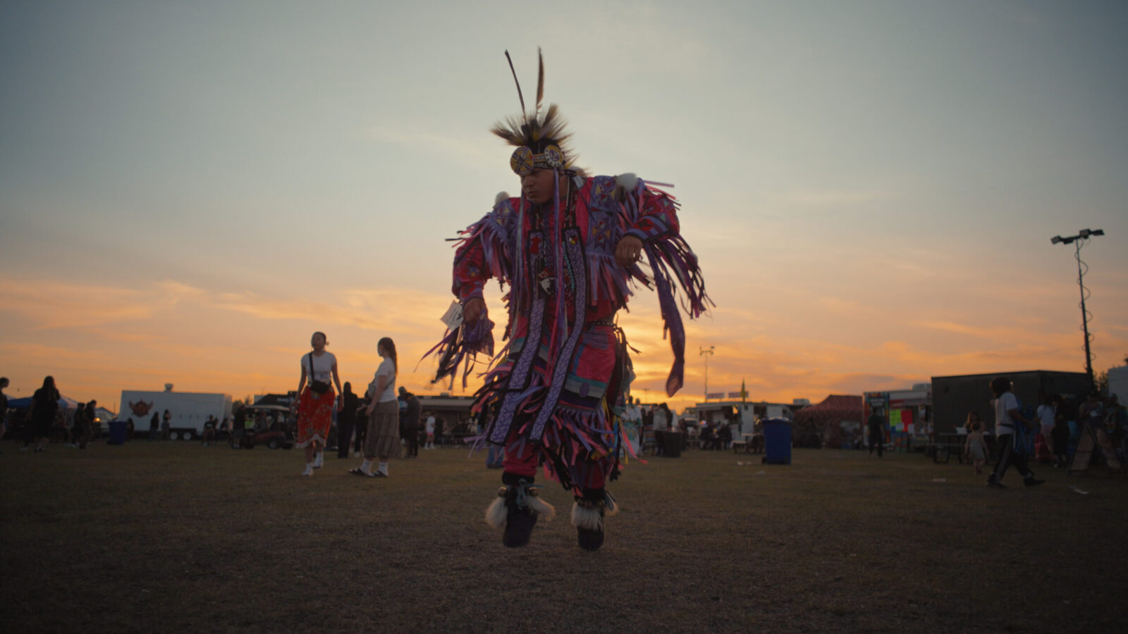 A man clad in cultural regalia dances with the sun setting in the backdrop