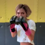 A young Afghan woman stands in a boxing stance with her fists raised, slightly obscuring her face.