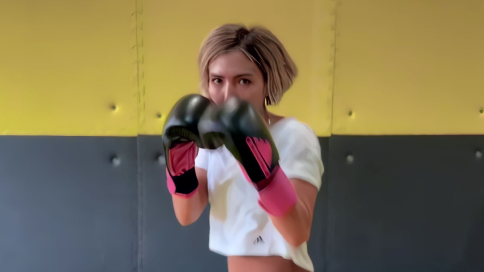 A young Afghan woman stands in a boxing stance with her fists raised, slightly obscuring her face.